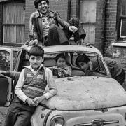 Children at play by derelict car dumped at Fieldgate Mansions in Whitechapel that David snapped in the 1970s